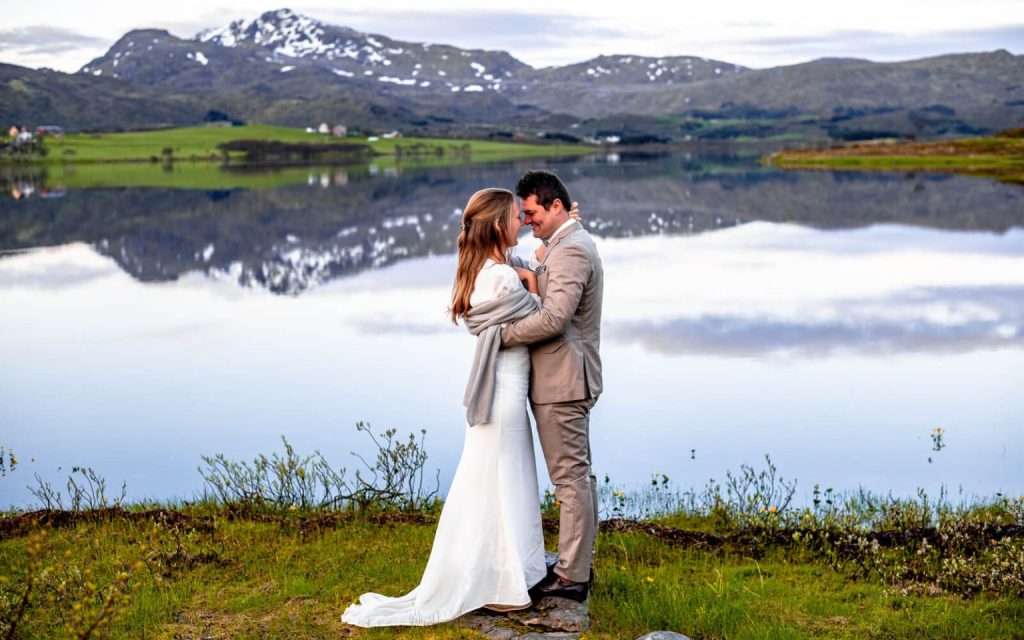 A freshly married couple with a background of mirror like scenery thanks to a lake at Lofoten islands